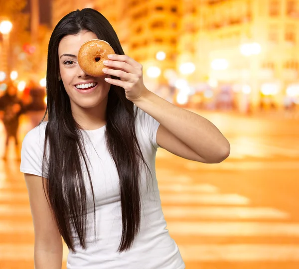 Portrait of young woman looking through a donut at city by night — Stock Photo, Image