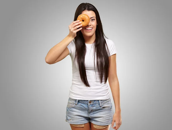 Porträtt av ung kvinna tittar genom en donut över grå — Stockfoto