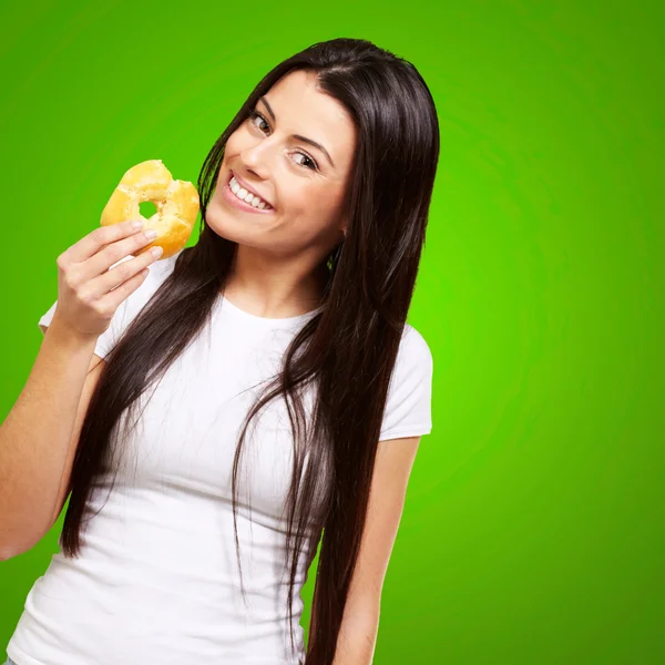 Retrato de una mujer joven comiendo una dona sobre verde — Foto de Stock