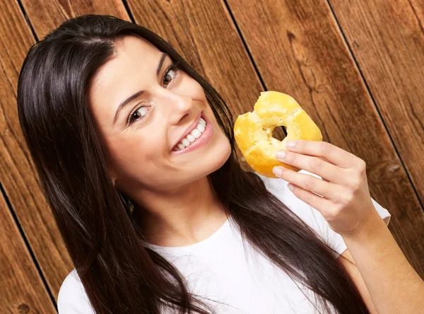 Portrait of young woman eating a donut against a wooden wall — Stock Photo, Image