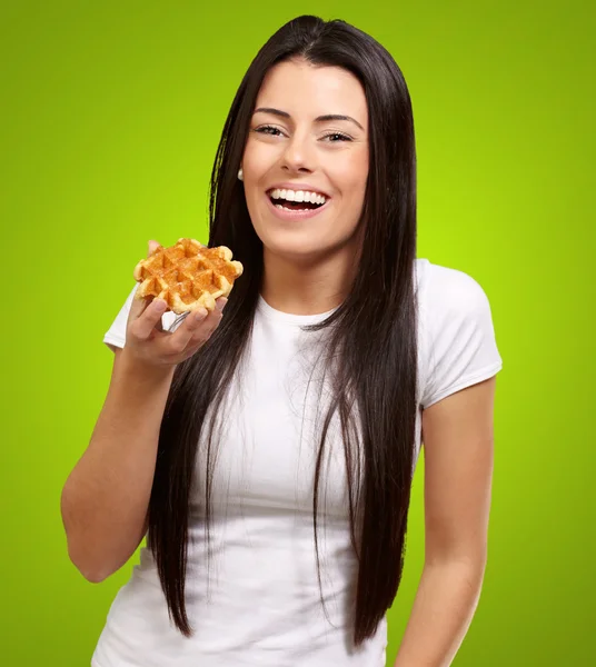 Portrait of young woman holding waffle over green background — Stock Photo, Image