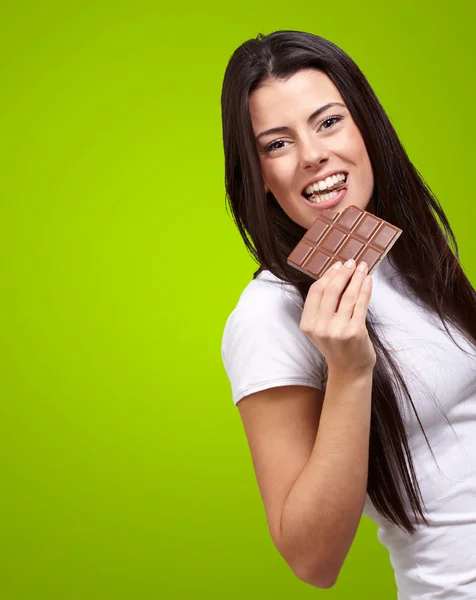 Portrait of young woman eating chocolate bar against a green bac — Stock Photo, Image
