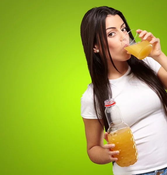 Portrait of young girl drinking orange juice against a green bac — Stock Photo, Image