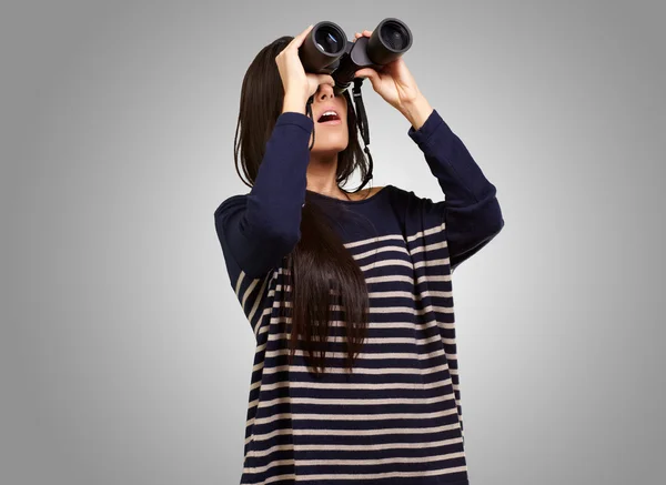 Portrait of young girl looking through a binoculars over grey — Stock Photo, Image