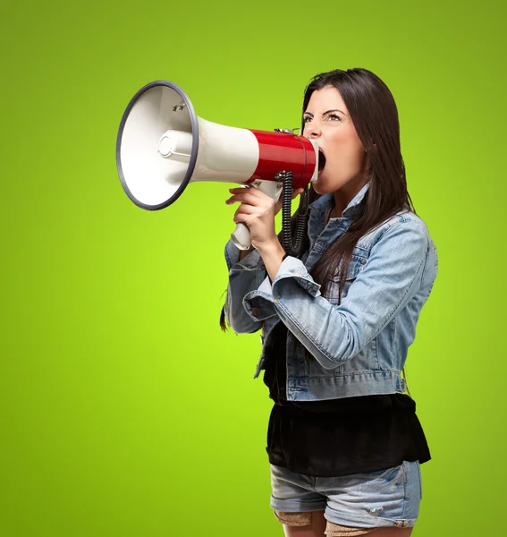 Portrait of young woman screaming with megaphone against a green — Stock Photo, Image