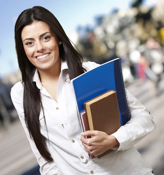 Mujer joven bonita sonriendo y sosteniendo cuadernos contra un stree — Foto de Stock