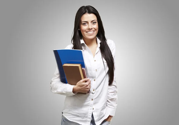 Junge Studentin hält Bücher in der Hand und lächelt vor grauem Hintergrund — Stockfoto