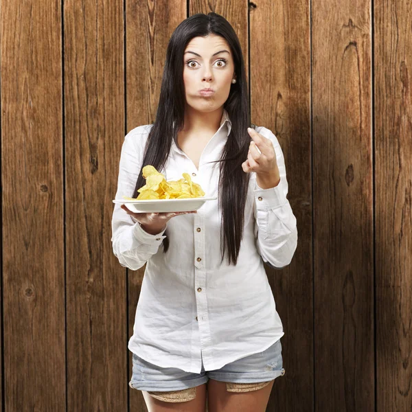 Mladá žena jíst brambůrky na dřevěné pozadí — Stock fotografie