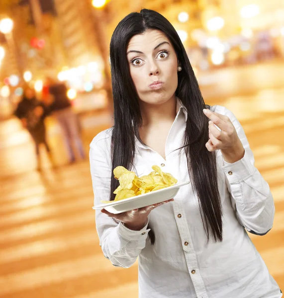 Mladá žena jíst brambůrky pozadí na noční město — Stock fotografie