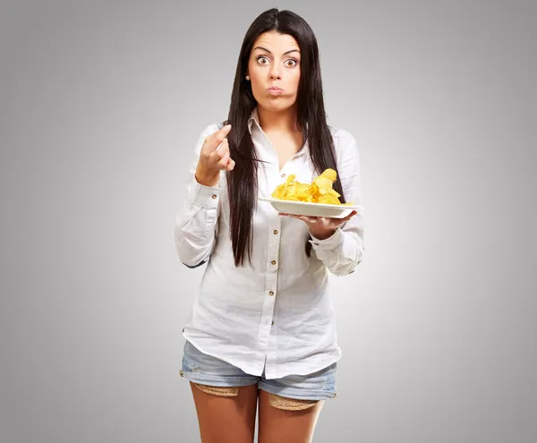 Молодая женщина ест картофельные чипсы на сером фоне — стоковое фото