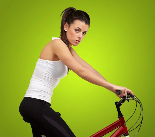 Yeşil arka plan üzerinde Bisiklete binme genç bir kadın portresi — Stok fotoğraf