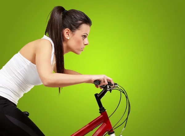 年轻的运动型女孩，骑自行车在绿色背景 — 图库照片