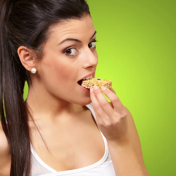 Jovem menina saudável comer uma barra de cereais sobre fundo verde — Fotografia de Stock