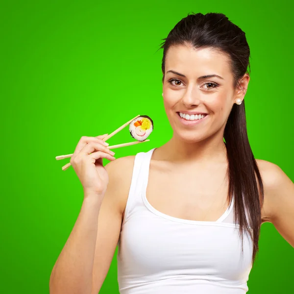Mujer joven sosteniendo un pedazo de sushi con palillos contra un g — Foto de Stock