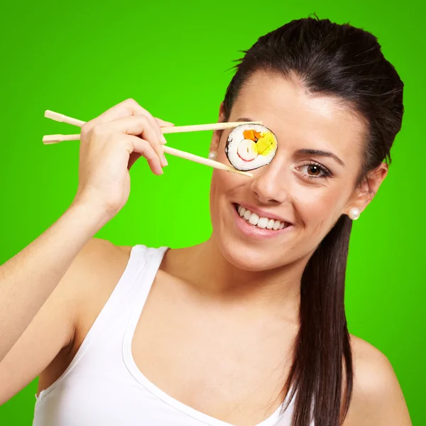 Jonge vrouw die betrekking hebben op haar oog met een sushi stuk tegen een groene — Stockfoto