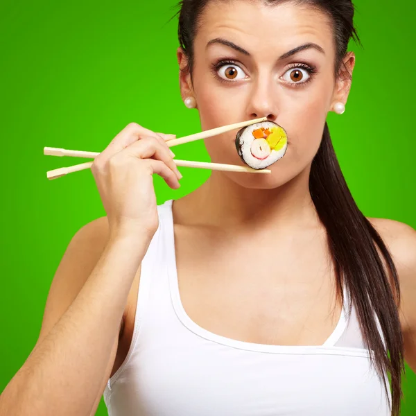 Young woman covering her mouth with a sushi piece against a gree — Stock Photo, Image