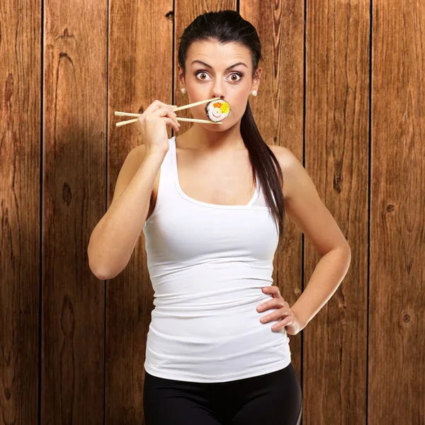 Giovane donna che copre la bocca con un pezzo di sushi contro un legno — Foto Stock