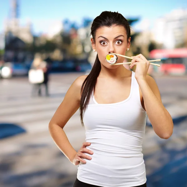 Young woman covering her mouth with a sushi piece against a stre — Stock Photo, Image