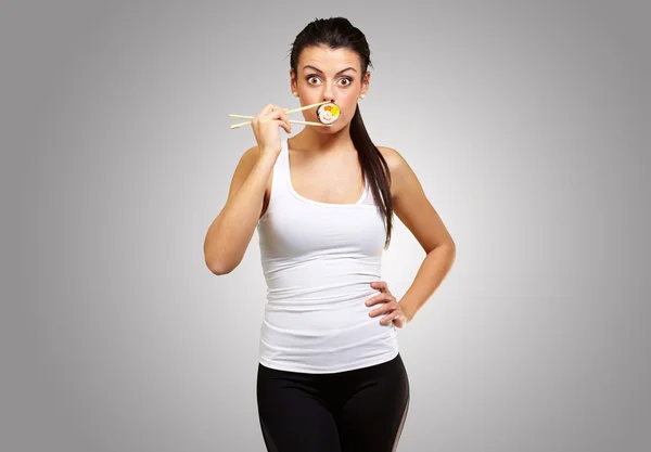 Ung kvinna som täcker hennes mun med en sushi bit mot en grå — Stockfoto