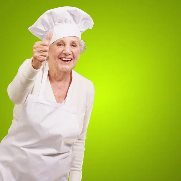 Portrait of cook senior woman doing approval gesture over green Stock Photo