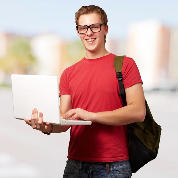 Portrait of young man holding laptop and wearing backpack at cit Obrazek Stockowy
