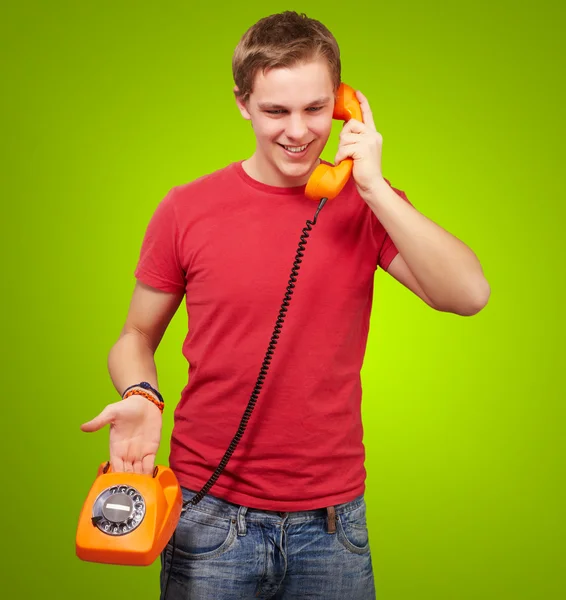 Portrait of young man talking on vintage telephone over green ba Stock Image