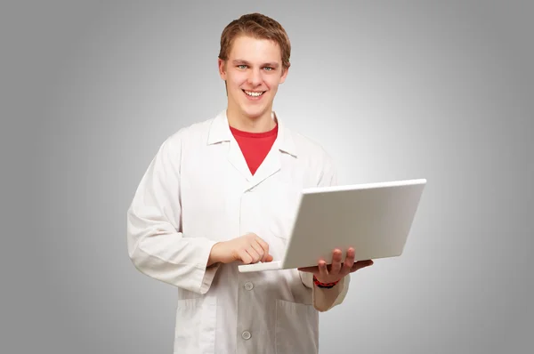 Portrait of young student holding laptop over grey background Stock Image