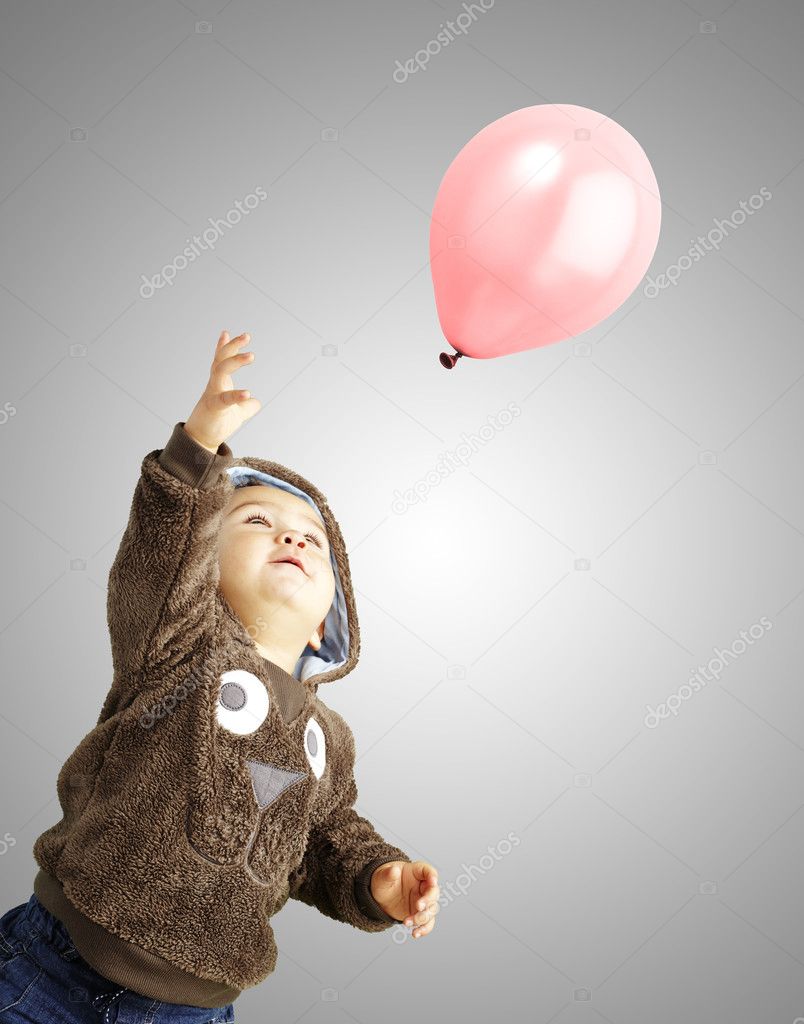 Portrait of funny kid trying to hold a pink balloon over grey ba
