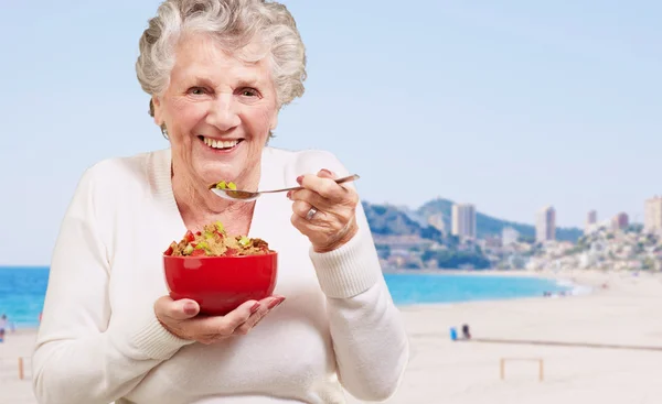 Retrato de una mujer mayor sana sosteniendo un tazón de cereales contra un —  Fotos de Stock