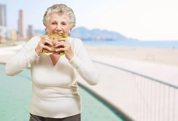 Starszy kobieta gryzienie zdrową kanapkę w pobliżu plaży — Zdjęcie stockowe