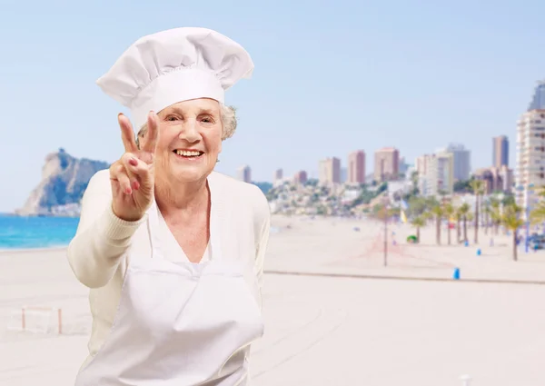 Portret kobiety starszy kucharz robi dobry gest przeciwko plaży — Zdjęcie stockowe