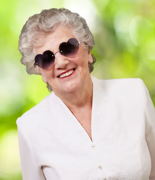 Portrait of happy senior woman wearing heart glasses against a n — Stock Photo, Image