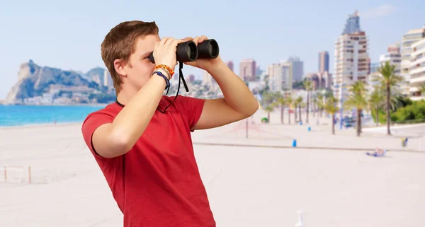 Porträt eines jungen Mannes, der am Strand durch ein Fernglas blickt — Stockfoto