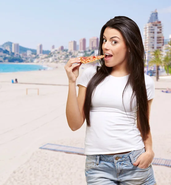 Porträt einer jungen Frau, die Pizza am Strand isst — Stockfoto