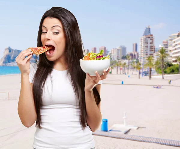 Портрет молодой женщины, поедающей пиццу и смотрящей салат в би — стоковое фото