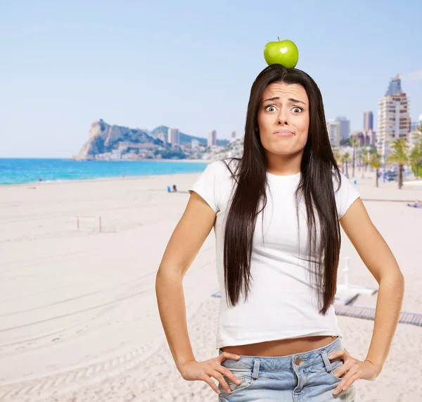 Retrato de mujer joven sosteniendo manzana verde en la cabeza contra un ser —  Fotos de Stock