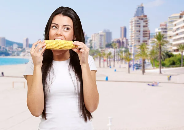 Portrait d'une jeune femme mangeant du maïs en épi contre la plage — Photo