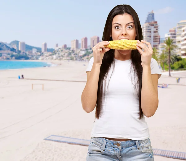 ビーチに対してコーンコブを食べる若い女性の肖像画 — ストック写真