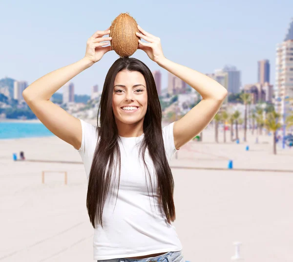 Portrét mladé ženy držící kokos proti pláži — Stock fotografie
