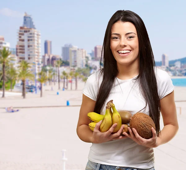 Retrato de una joven sosteniendo frutas tropicales contra la playa —  Fotos de Stock
