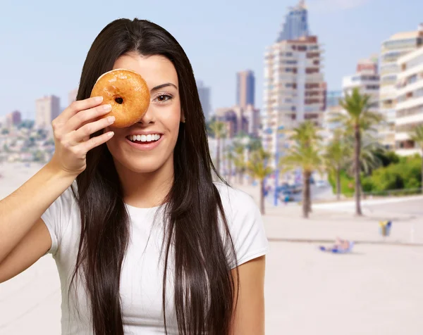 Portrait of young woman holding donut in front of her eye agains — Stock Photo, Image