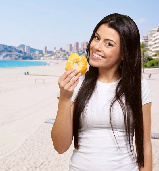 Retrato de mujer joven sosteniendo donut contra la playa —  Fotos de Stock