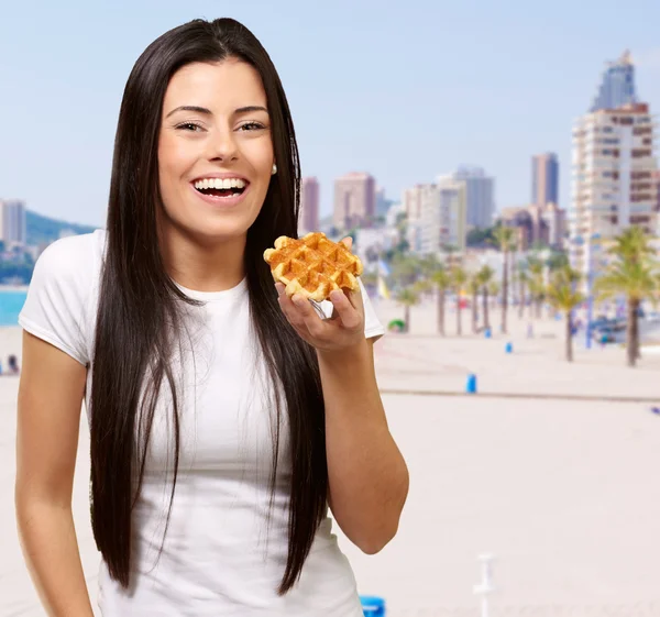 Portrait of young woman holding waffle against a beach — Stock Photo, Image