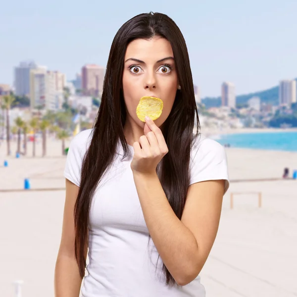 Portrait of young woman holding potato chip on her mouth against — Stock Photo, Image