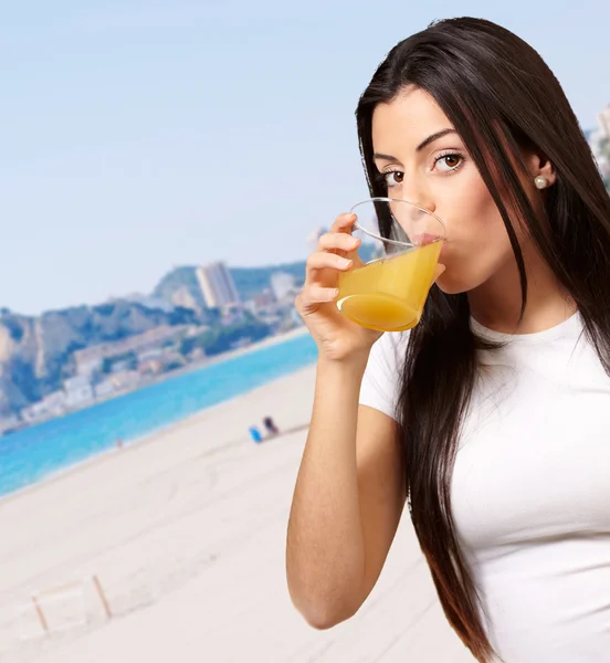 Portrait of young girl drinking orange juice against a beach — Stock Photo, Image