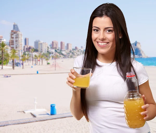 Retrato de menina bebendo suco de laranja contra uma praia — Fotografia de Stock