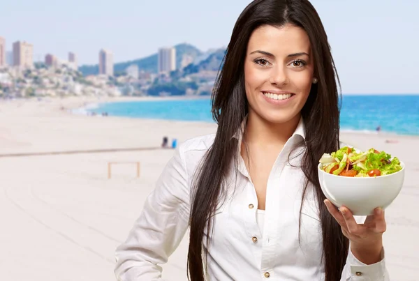 Retrato de una joven mujer sosteniendo ensalada contra una playa — Foto de Stock