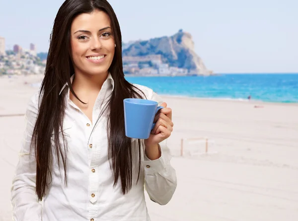 Joven chica sosteniendo taza contra una playa — Foto de Stock