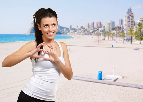 Porträtt av ung kvinna gör hjärtsymbol mot en strand — Stockfoto