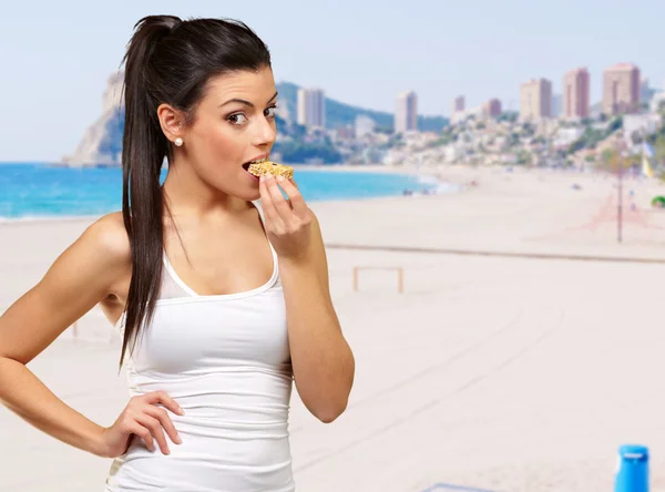 Young healthy girl eating a cereal bar against a coastline backg — Stock Photo, Image